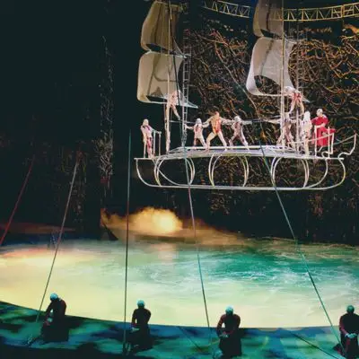 Performers on a ship-shaped platform suspended above a pool of water.