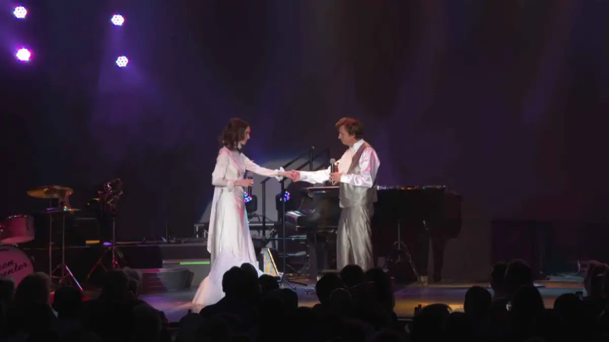 Karen and Richard Carpenter impersonators holding hands on stage while performing