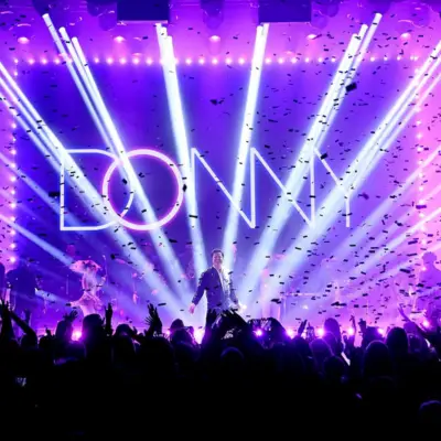 Donny Osmond stands on stage with confetti falling and bright lights shining behind him.