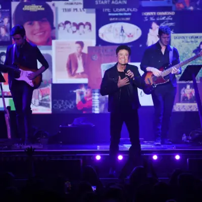 Donny Osmond performs on stage singing with two guitarists behind him.