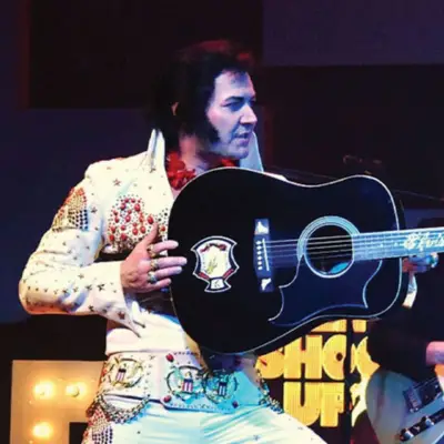 Elvis impersonator with his guitar posing on stage.