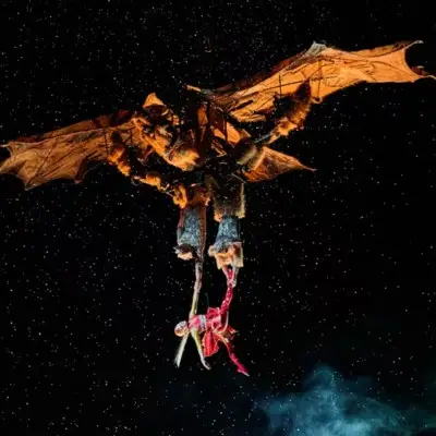 An aerial performer from Cirque du Soleil's KÀ suspended beneath a large, winged dragon.
