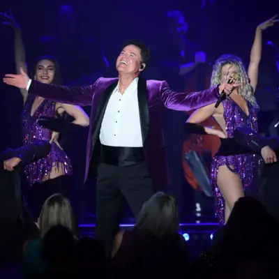 Donny Osmond performs on stage with two backup dancers behind him.