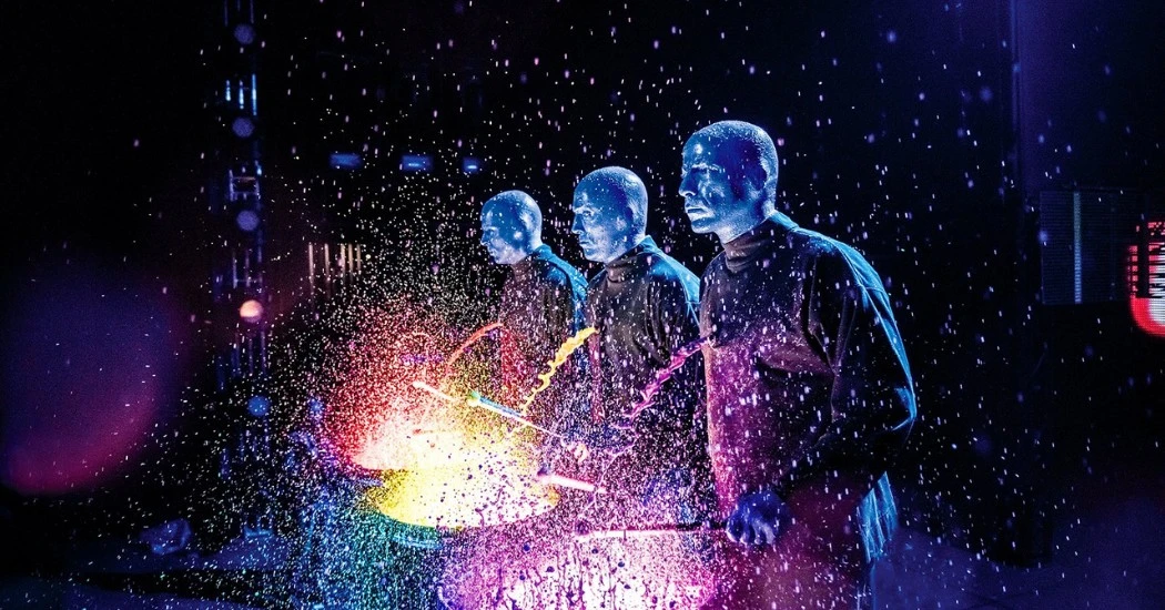 Blue Man Group performing with colorful paint splashes.