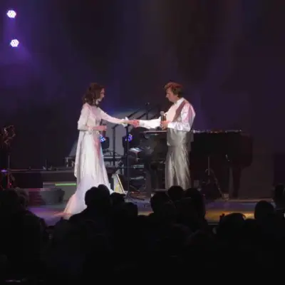 Karen and Richard Carpenter impersonators holding hands on stage while performing