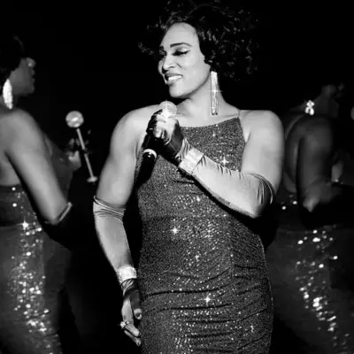 A close-up of All Motown singer performing on stage with the other singers blurred behind her in black and white.