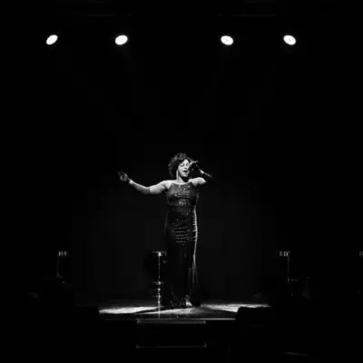 A singer from All Motown alone on stage singing under bright spotlights in black and white.