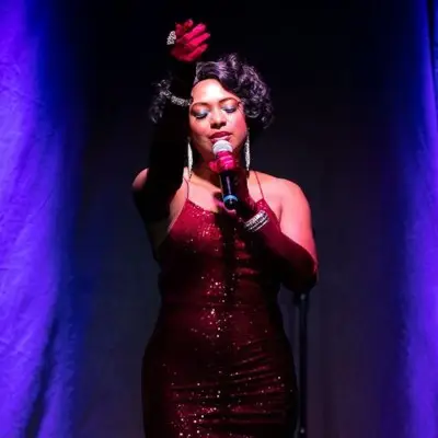 A close-up of All Motown singer wearing a red dress passionately sings on stage under colorful lights.