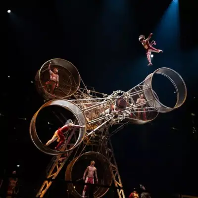 Acrobats performing inside and around a large rotating metal cage apparatus in KÀ by Cirque du Soleil.