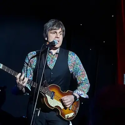 A member of Love Is All You Need on the stage playing the guitar and singing