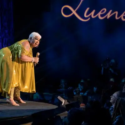 Luenell performing in front of the audience in a golden dress