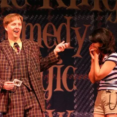 Mac King holding a deck of cards and a gasping audience member