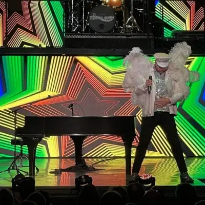 Piano Man performer wearing white feathered costume standing next to piano