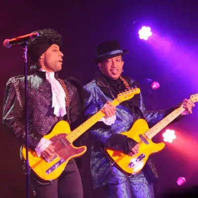 Two musicians wearing vintage style clothes play yellow guitars on stage