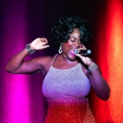 All Motown singer wearing a red and silver dress passionately sings on stage under colorful lights.
