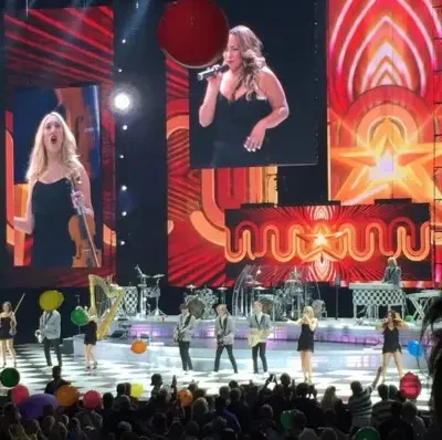The team members performing while they are projected on the screen at the Colosseum venue